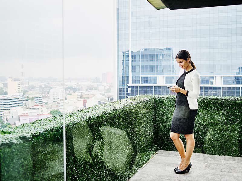 Smiling female business executive standing on office terrace looking at information on smartphone
